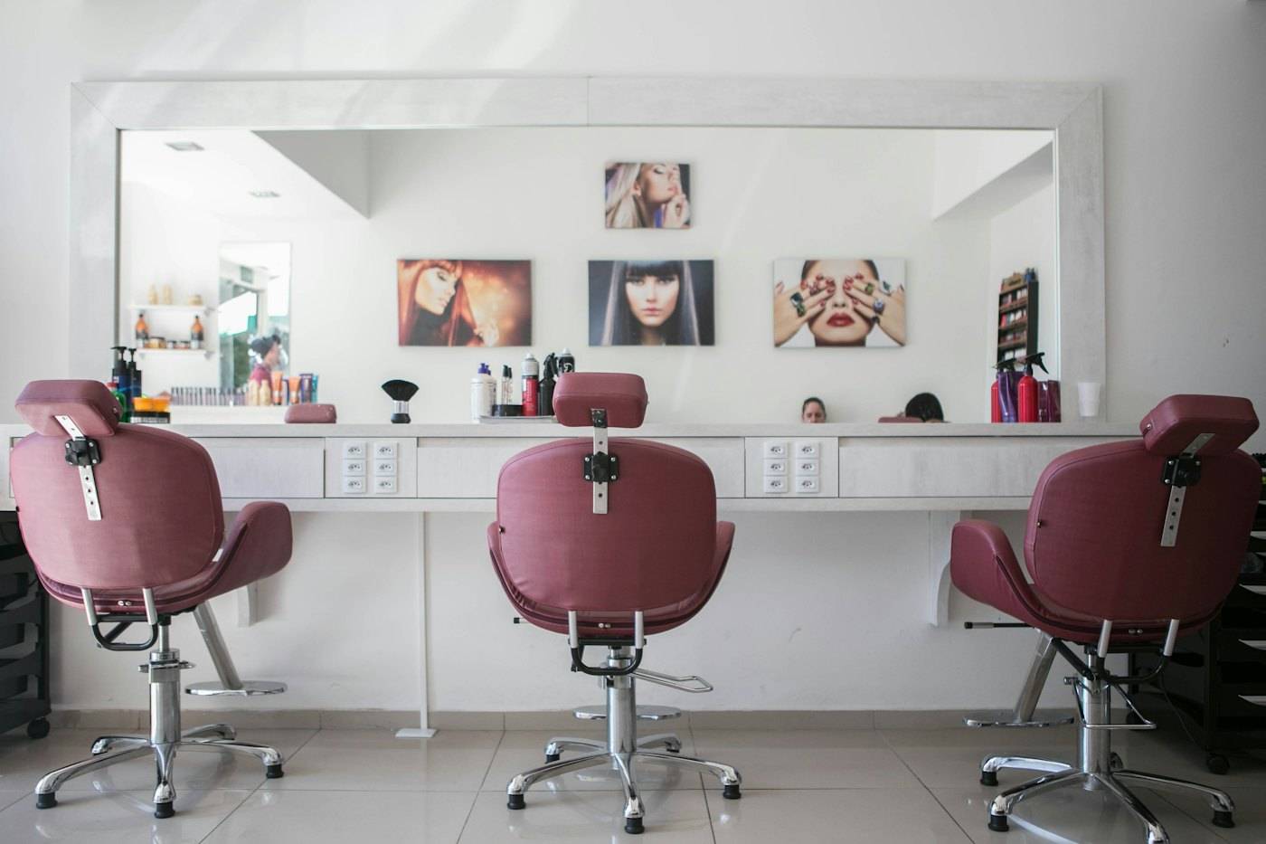 Beyaz tezgâh ve büyük ayna önünde mürdüm renkli üç salon koltuğu